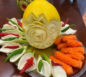 Na talerzu kwiat wyrzeźbiony w melonie. Wokół niego kwiaty z porów i papryki oraz szyszki z marchwi.