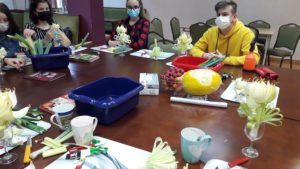 Uczniowie siedzą przy stole i rzeźbią w warzywach i owocach. Na stole  narzędzia służące do dekoracji.
