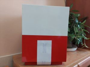 Na zdjęciu widoczna jest zapieczętowana urna w kolorach białym i czerwonym. 